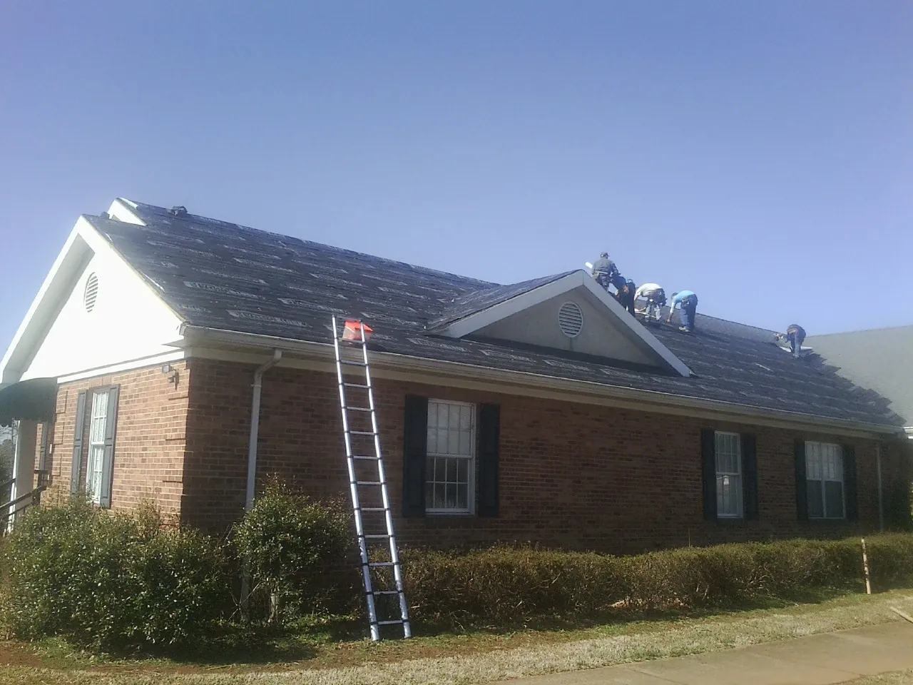 Crew tearing shingles off a brick ranch roof with a ladder set — Emergency Roof Repair work by our crew in Streetsboro
