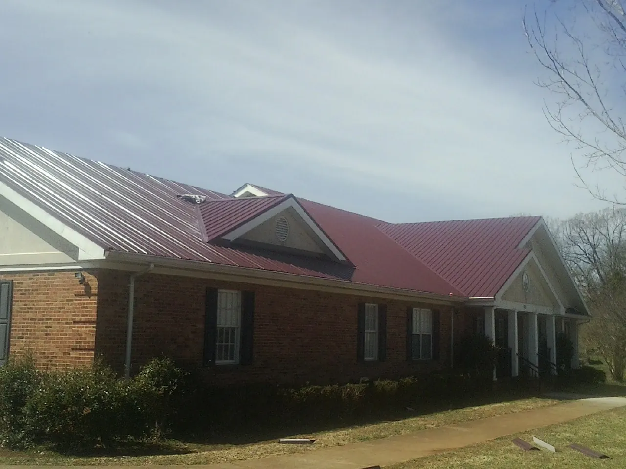 Red metal roof with gabled entries on a long brick building, from a Hail Damage Roof Repair job in Streetsboro