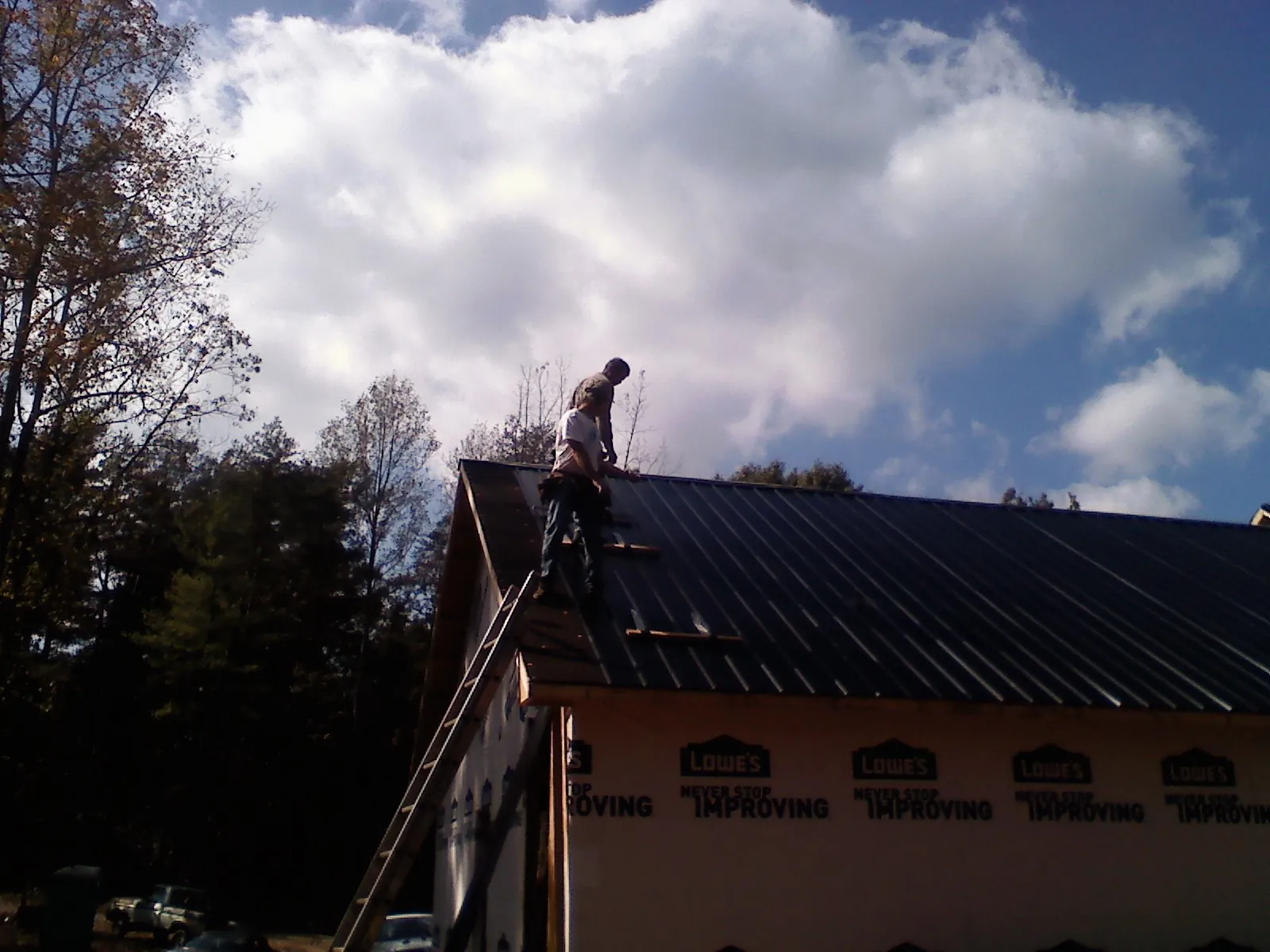Roofer fastening dark metal panels high against a cloudy sky, from a Roof Inspection job in Streetsboro