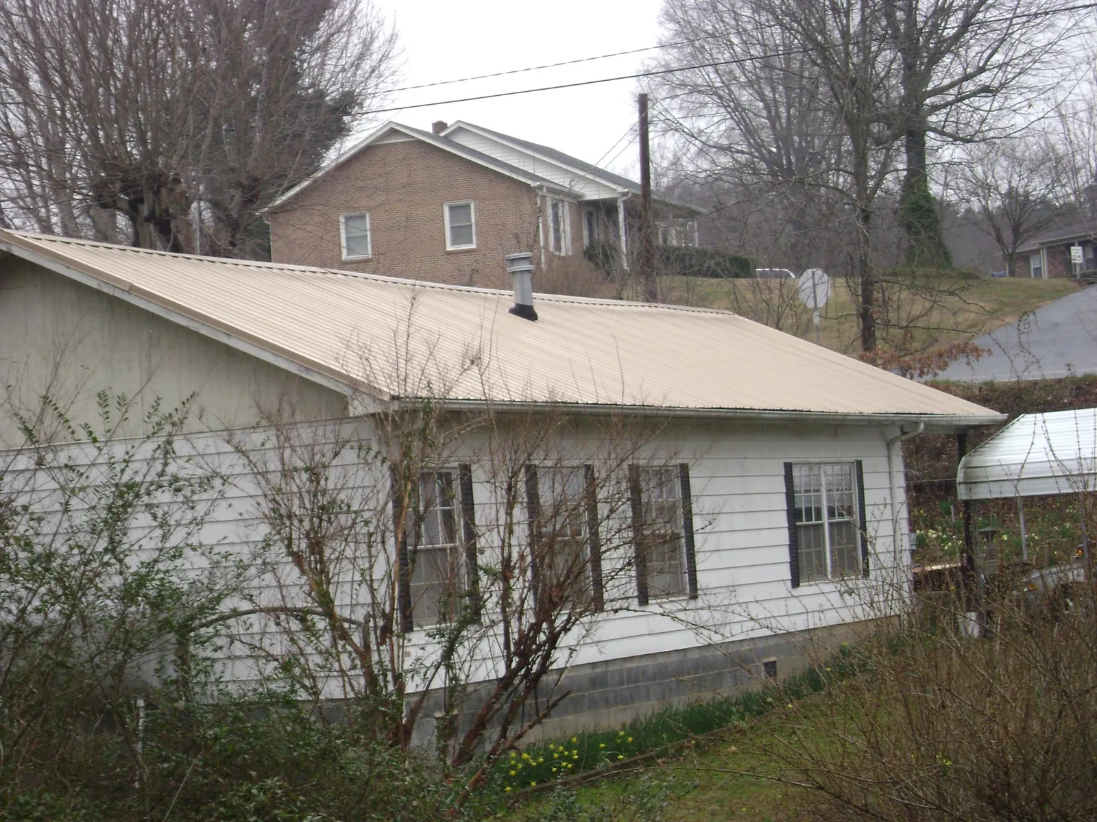 Tan metal roof on a white sided house set into a hillside — Commercial Roofing by Roofing Brothers in Streetsboro